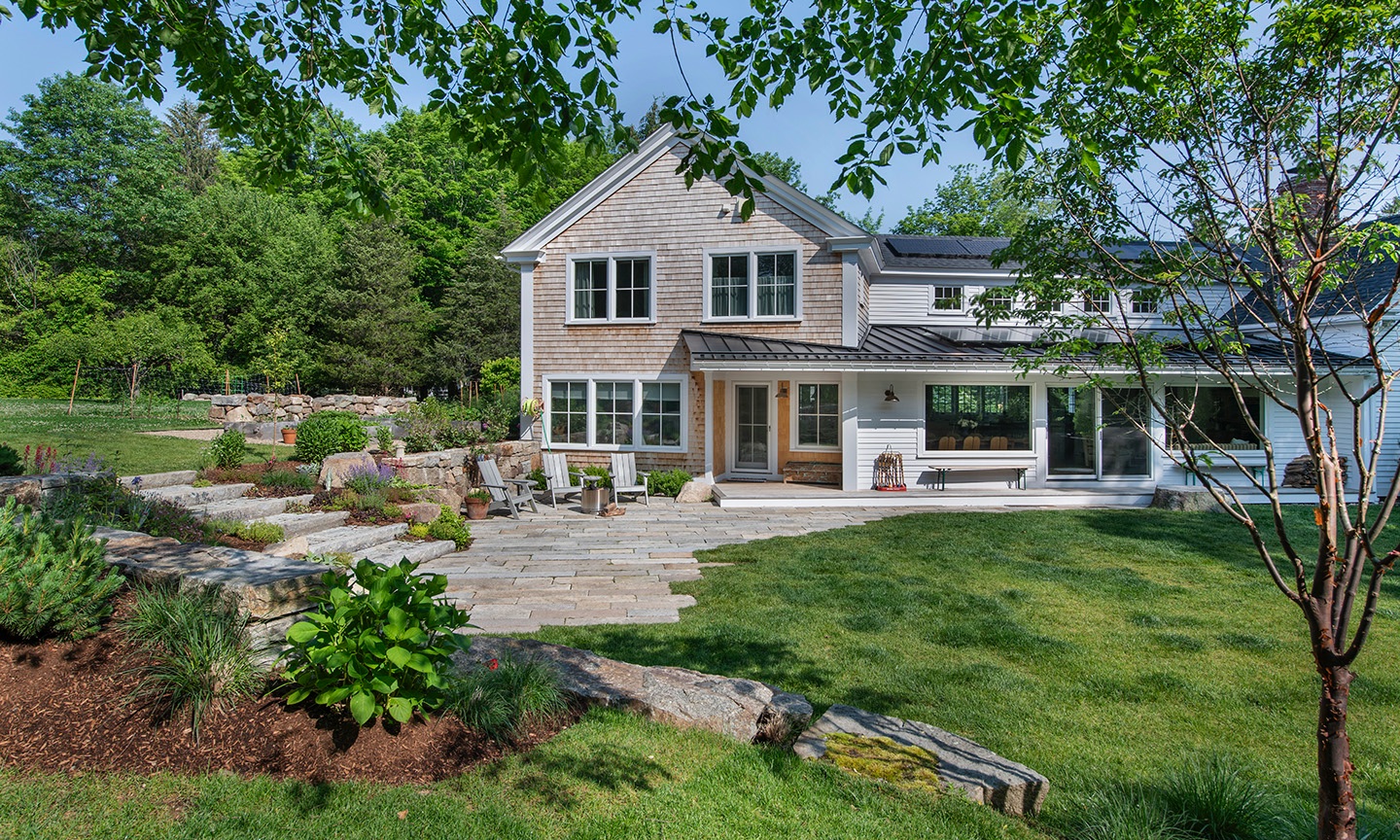Shingled farmhouse with a stone terrace and lawn by Benjamin Nutter Architects
