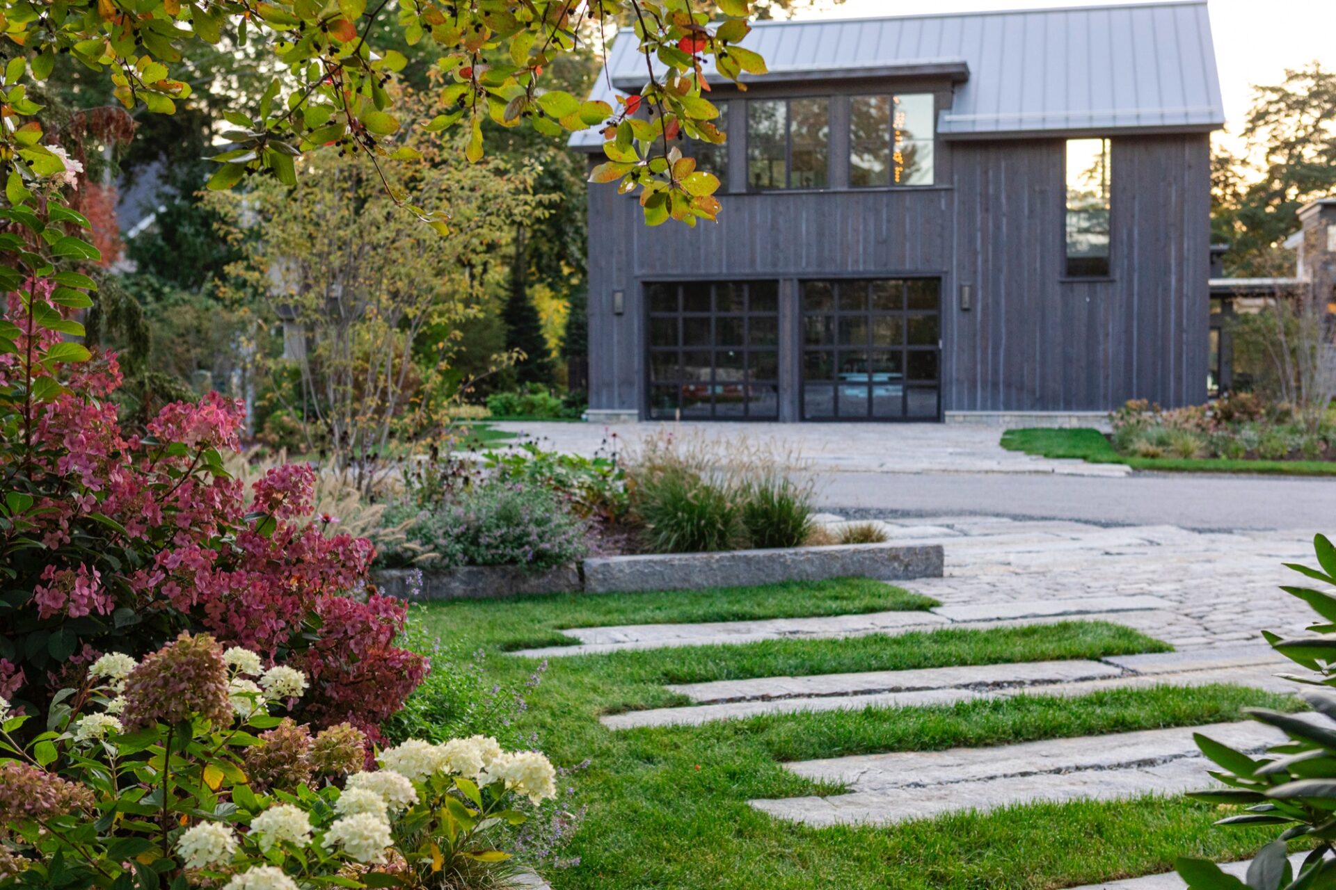 Stone path through gardens to a dark-clad barn in a landscape by Gregory Lombardi Design