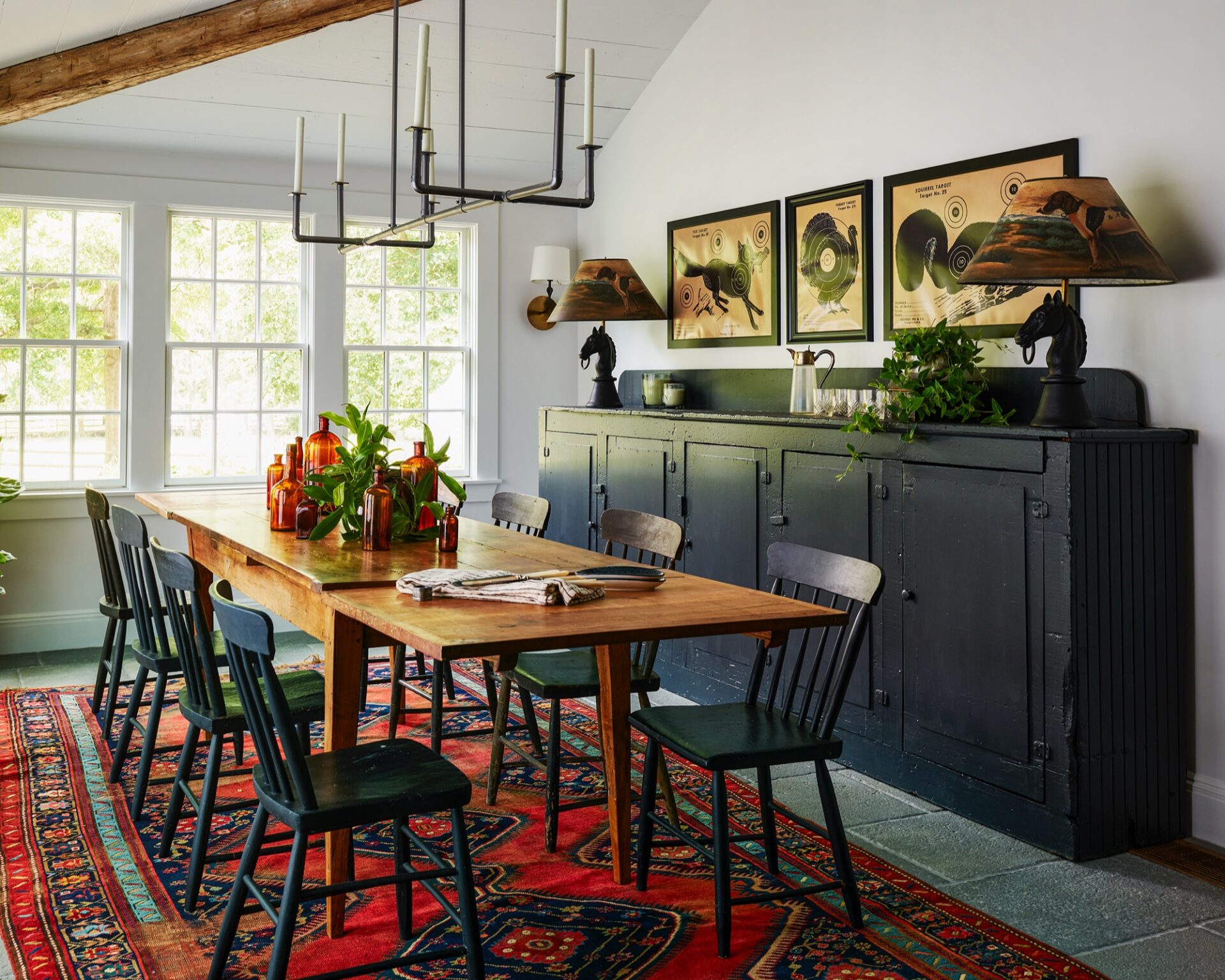 Dining room with a farmhouse table, black Windsor chairs, and a red rug by Kristina Crestin Design