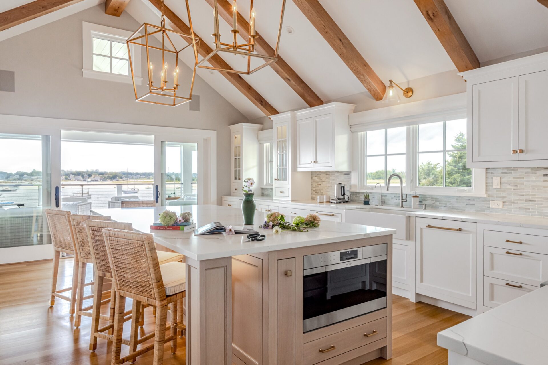 Waterfront kitchen with white cabinetry and woven counter stools by SV Design