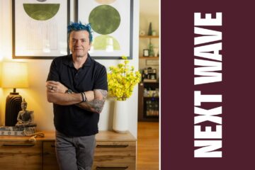 Jason Santos stands with his arms crossed in a restaurant beside vertical Next Wave lettering on maroon.