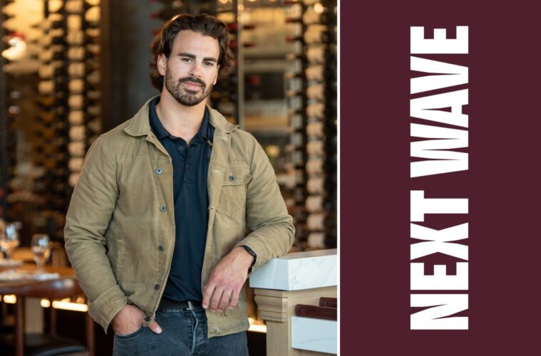 Max Faro leans against a counter with rows of wine bottles behind him beside vertical Next Wave lettering on maroon.