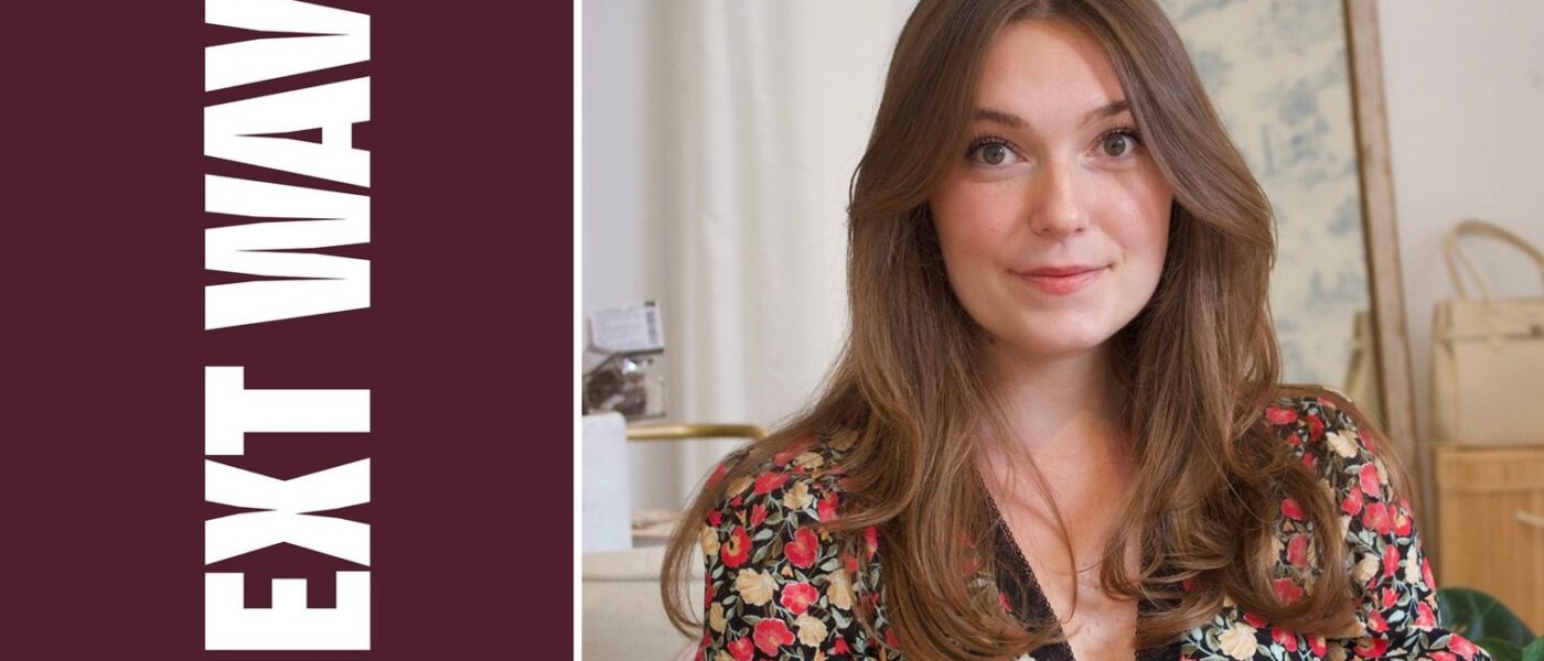 Ocean Lilly Otte wears a floral dress in her boutique beside vertical Next Wave lettering on maroon.