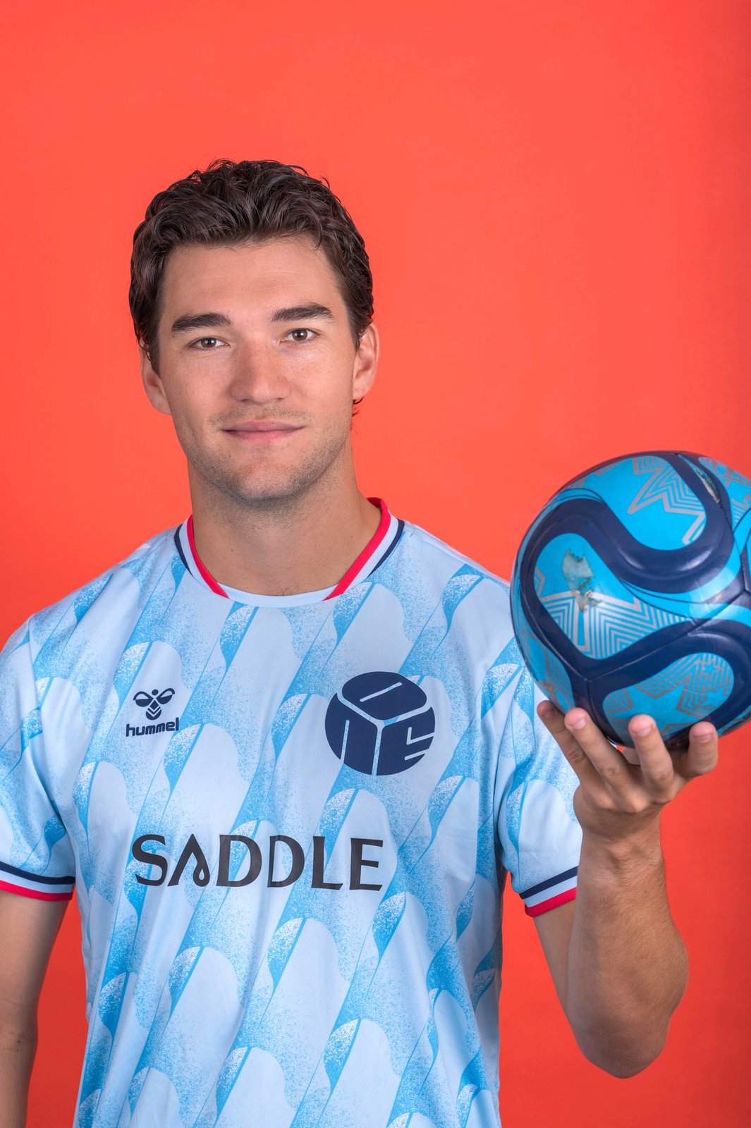 Robbie Robinson holds a soccer ball against an orange background.