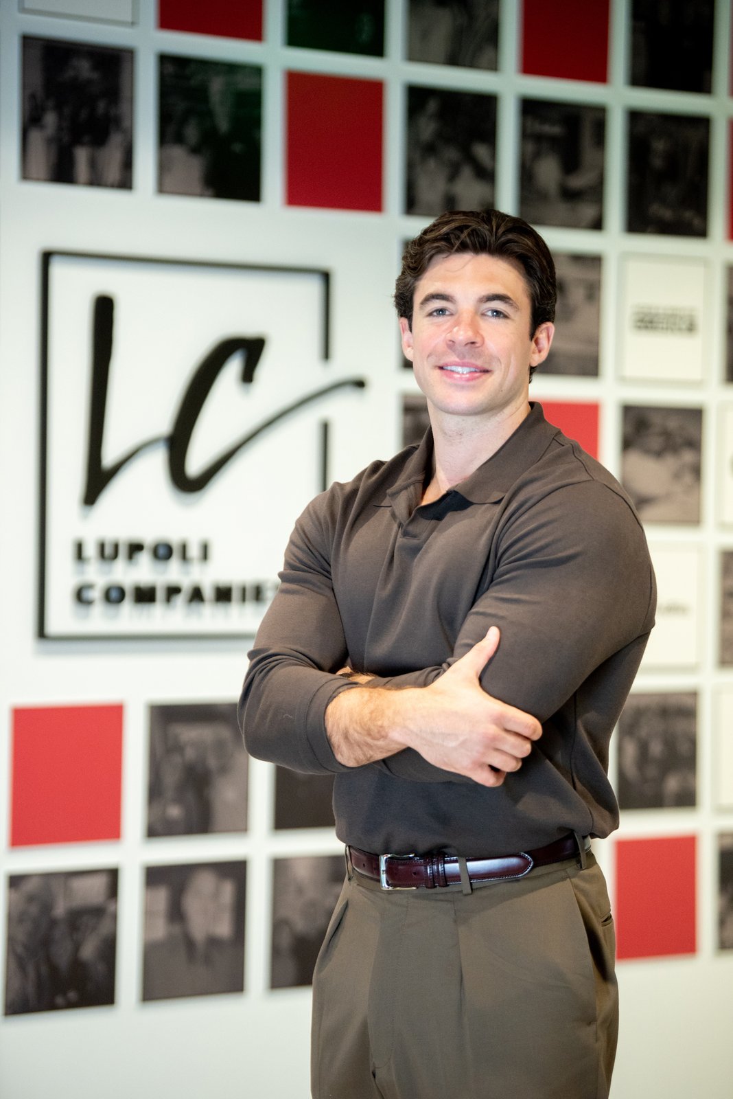 Sal Lupoli Jr. stands with his arms crossed in front of Lupoli Companies signage.